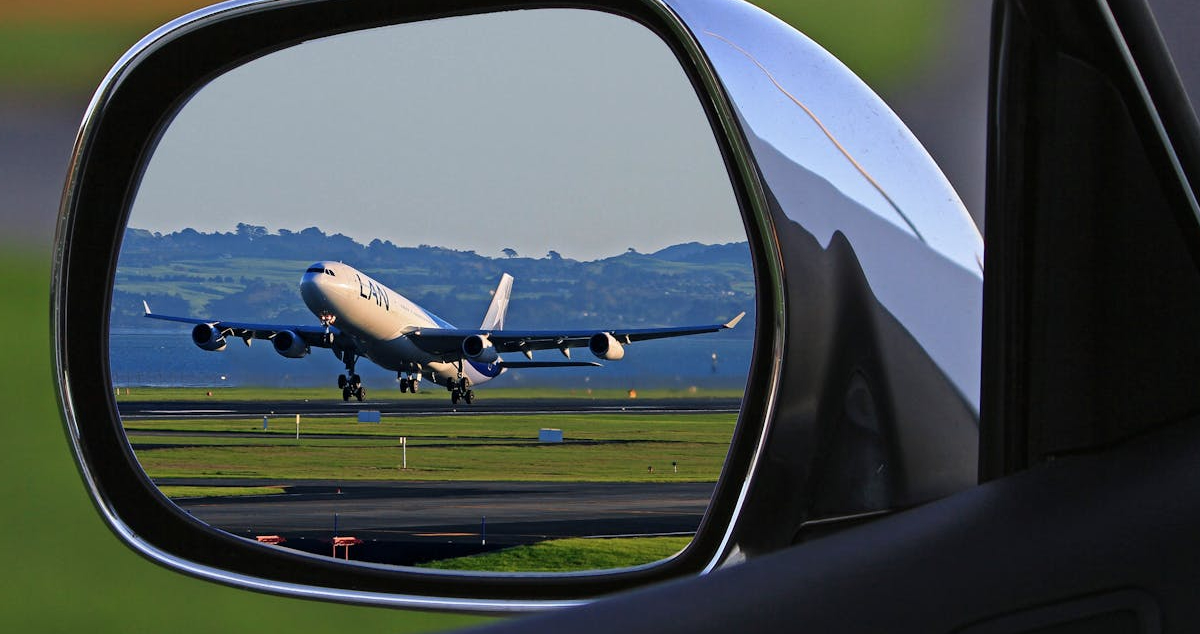 Car side mirror reflecting an airport runway with an airplane in the background,