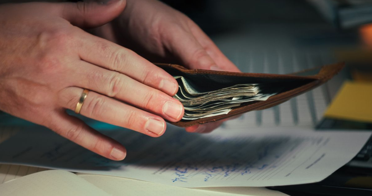 Person reviewing car rental terms and conditions while holding a wallet with cash before booking a rental car